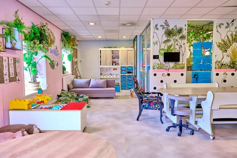 Lichte groepsruimte bij kinderdagverblijf Doortje met planten, een bank en speeltafels